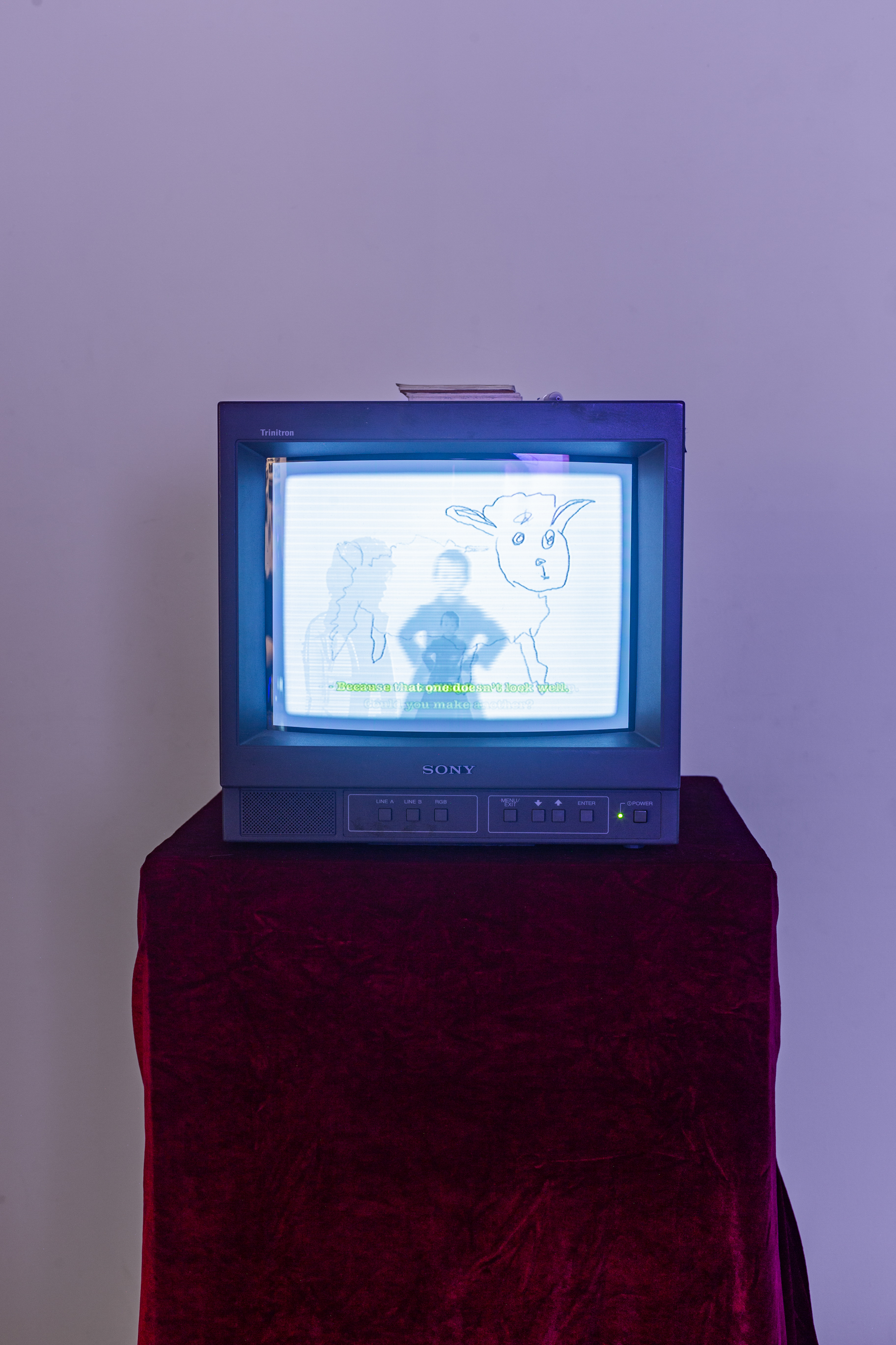 A CRT tv with artistic visuals on it, ontop of a podium covered in a table cloth in a white room.